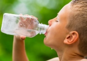 Boy drinking water outdoors from water bottle.