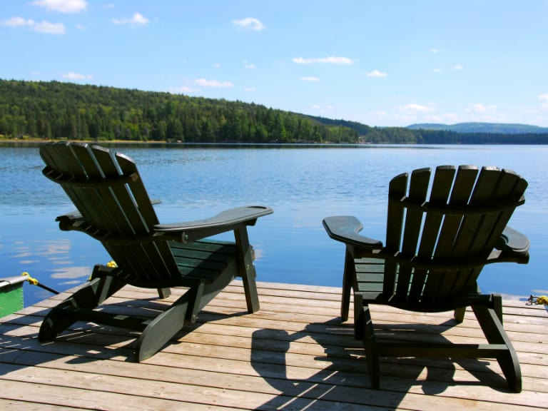 Muskoka chairs on a dock over looking lake.