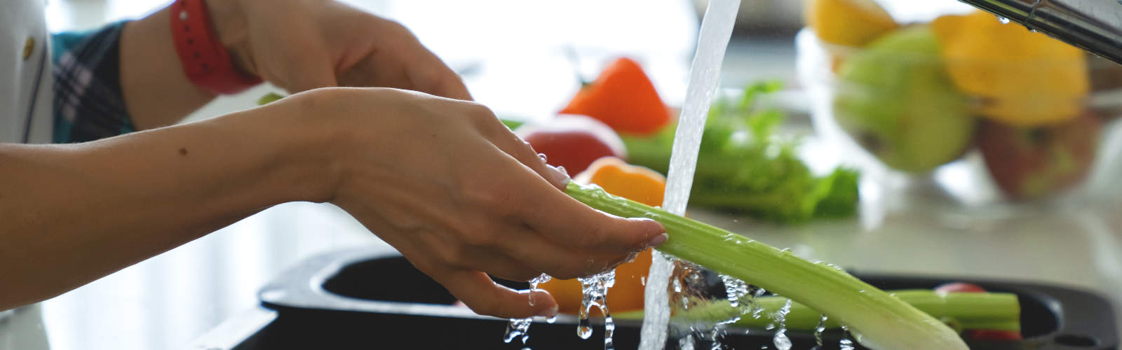 Woman washing vegetables in kitchen sink.